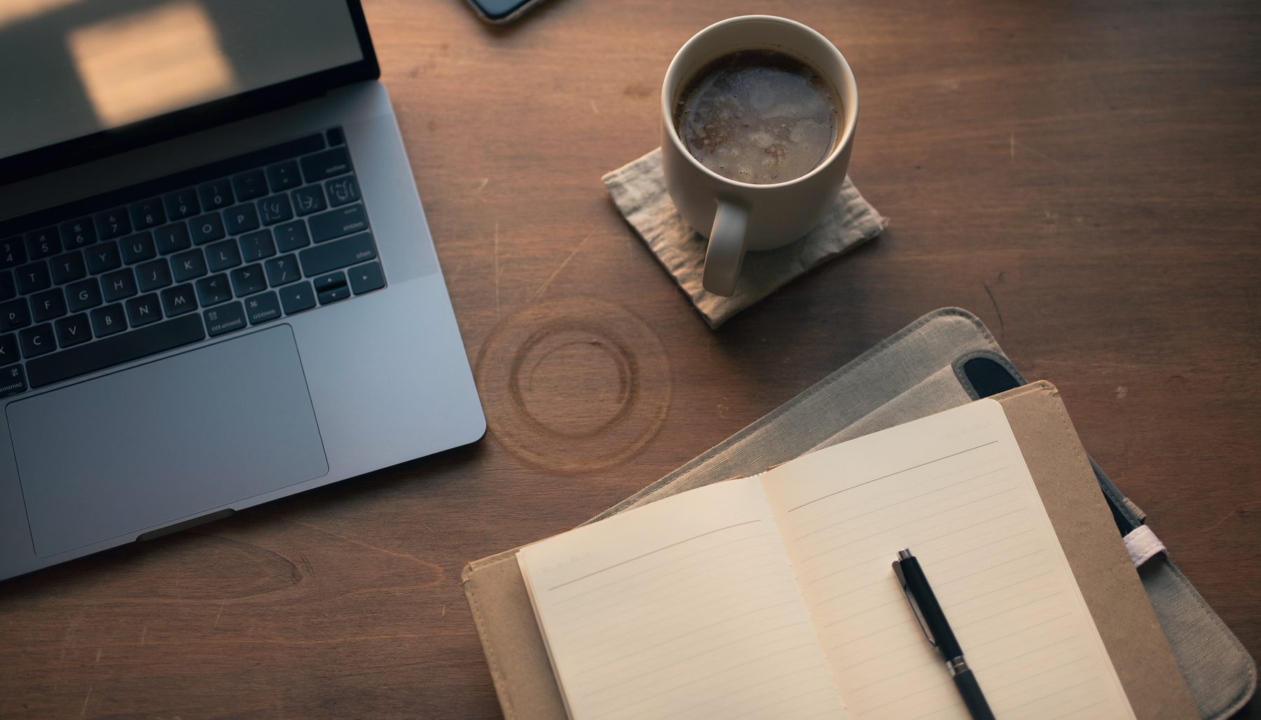 A desk with a laptop, notebook and cup of coffee